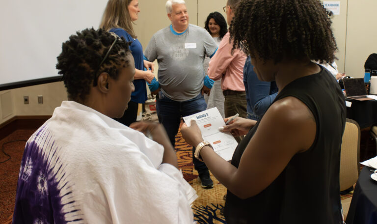 Two people standing, speaking and looking at a document. 